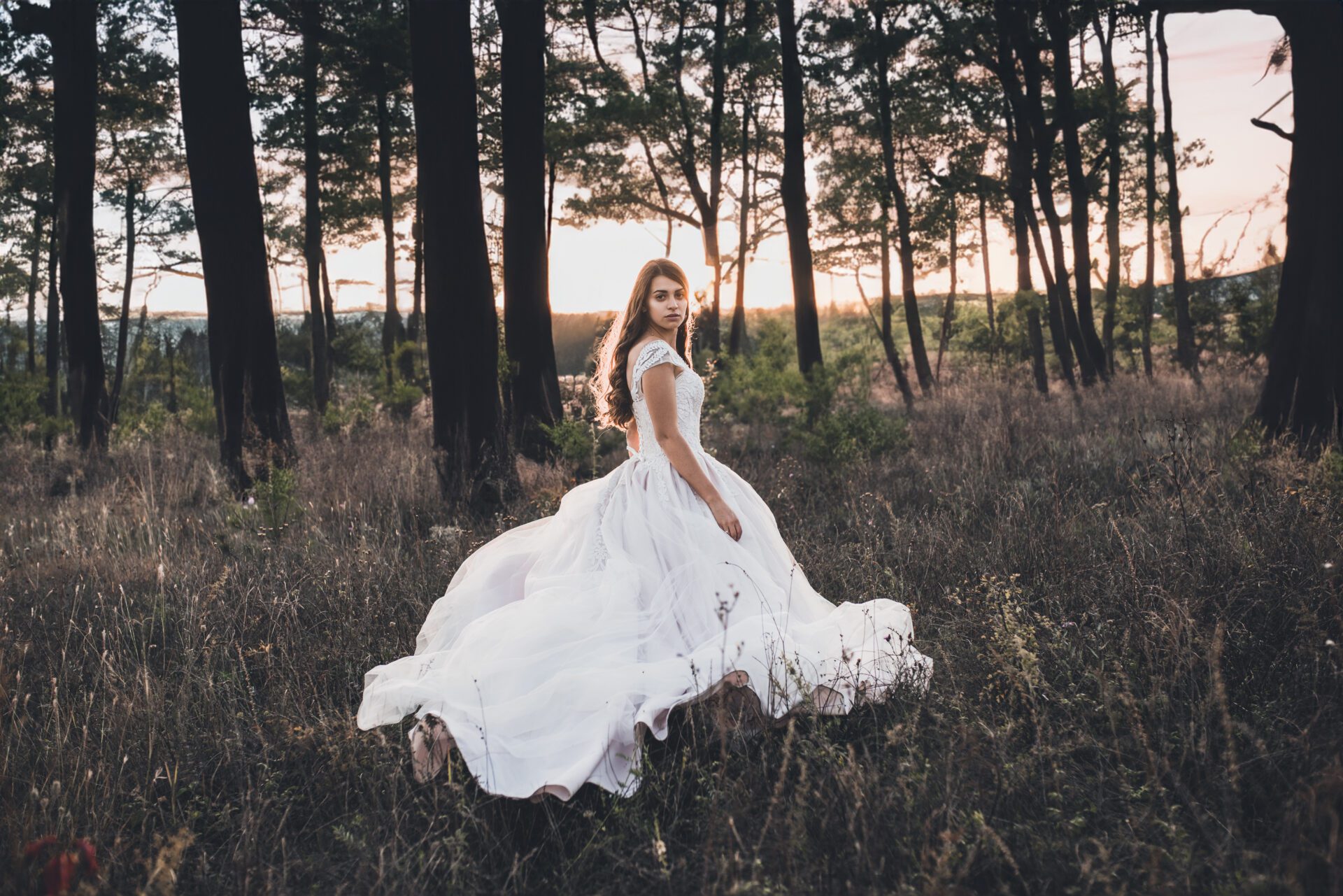 Bride in wedding white dress walking on the meadow in summer at sunset