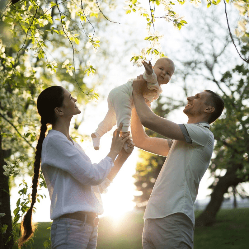 Happy man and woman playing with baby outdoors.